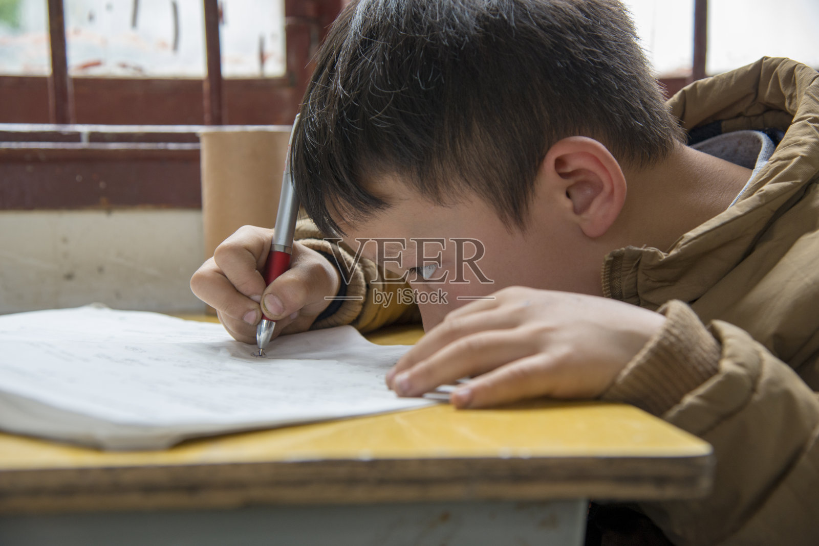 中国男孩在学校工作，高度集中在小洞村，黄刚，一个中国男孩的面部画像。拿着钢笔的男孩正在学校里写字。黄刚，中国贵州省侗族小村。照片摄影图片