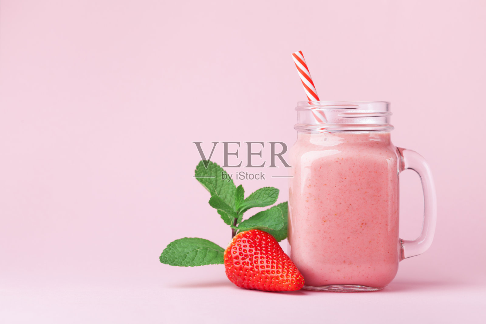 草莓冰沙或奶昔在梅森瓶装饰薄荷在粉红色的桌子。吃健康的早餐和零食。照片摄影图片