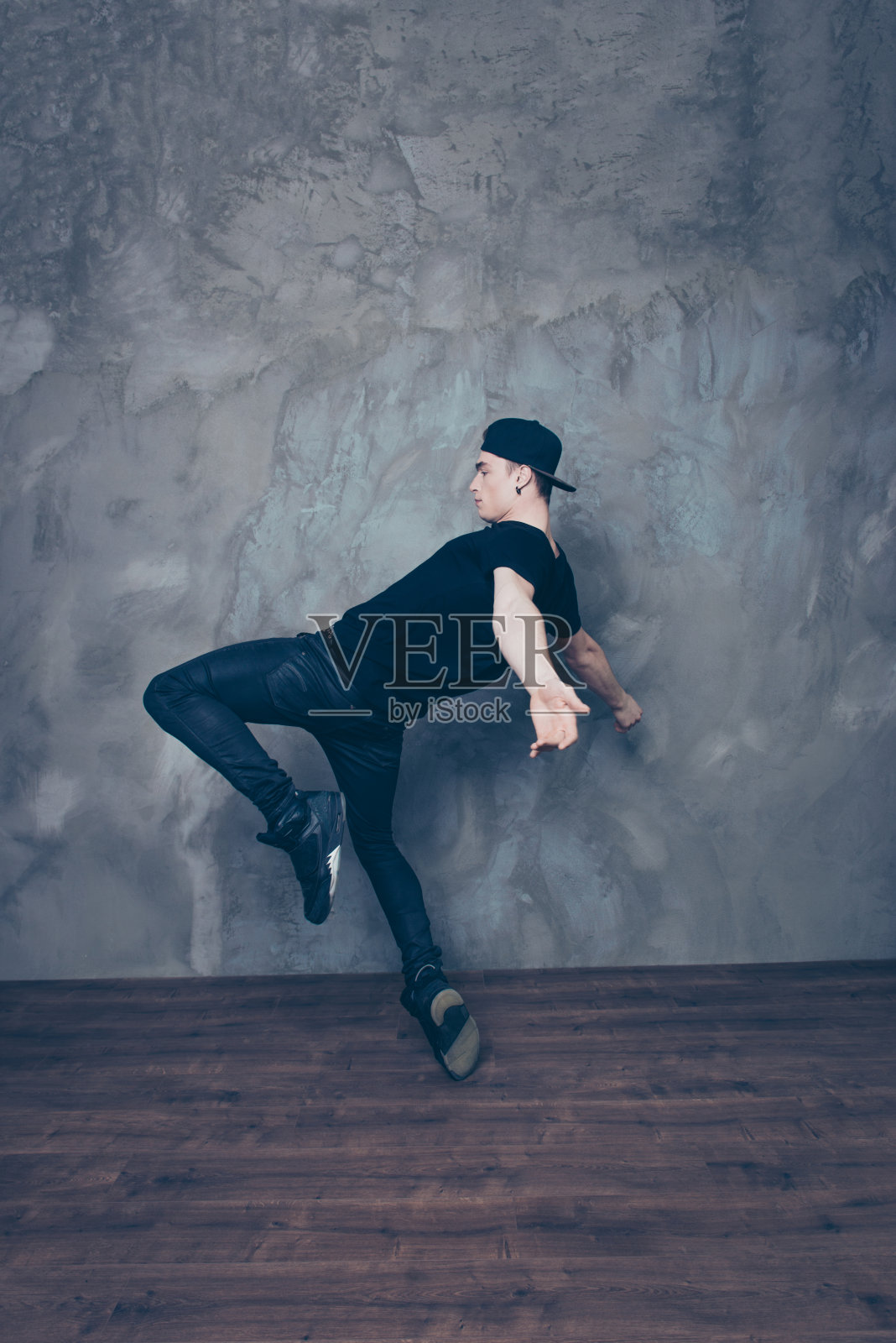 年轻的现代舞者在舞蹈时在工作室背景上摆姿势。他穿着黑色的衣服照片摄影图片