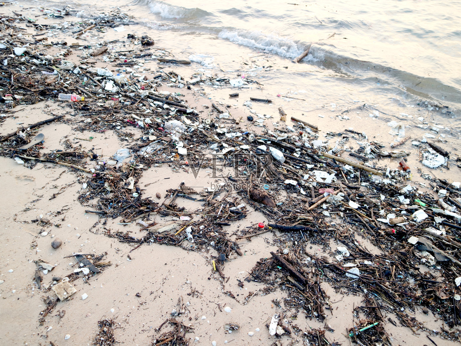 瓶子、玻璃、泡沫、竹子和海滩上的废物污染照片摄影图片