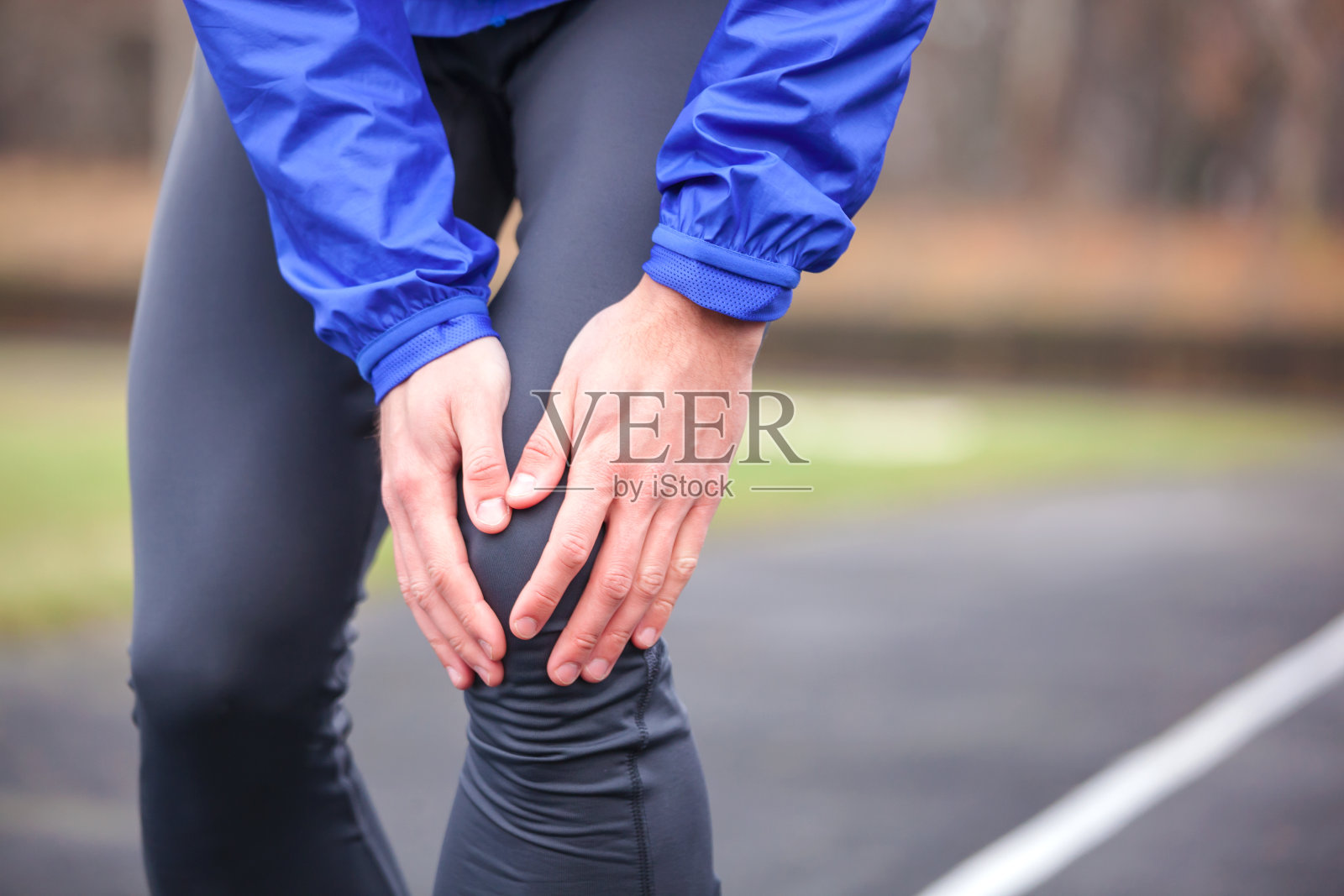 一个年轻的跑步者在跑步时抱着他受伤的膝盖。照片摄影图片