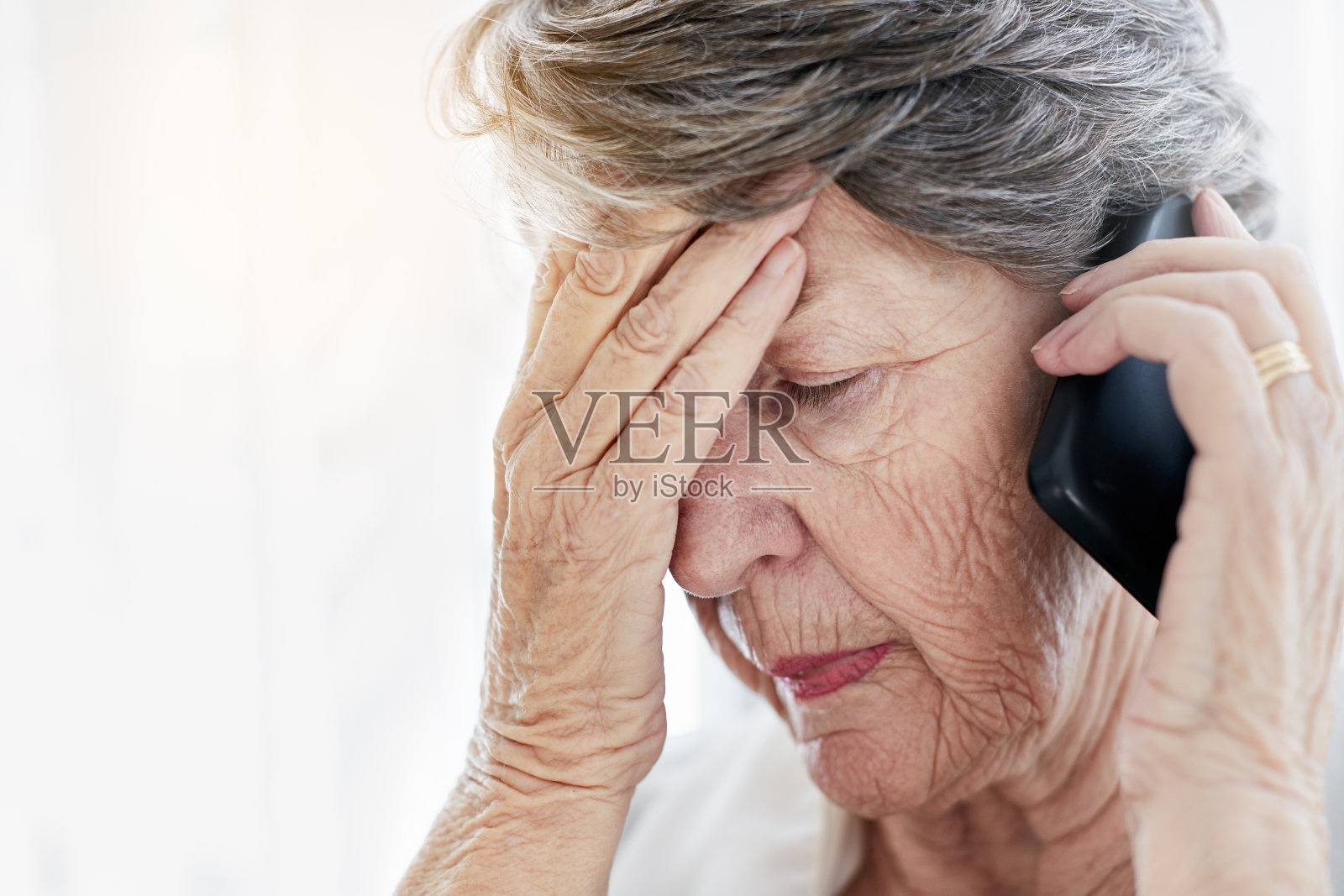 拿着手机的老妇人闭上眼睛，一副心烦意乱的样子照片摄影图片