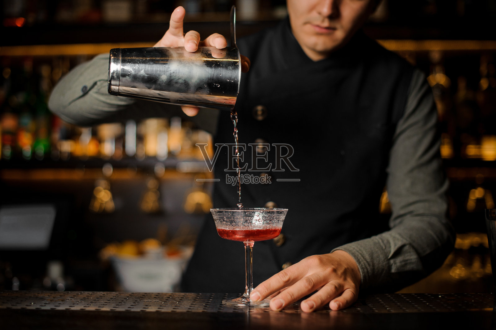酒保将含有金巴利的酒精饮料倒入鸡尾酒杯照片摄影图片