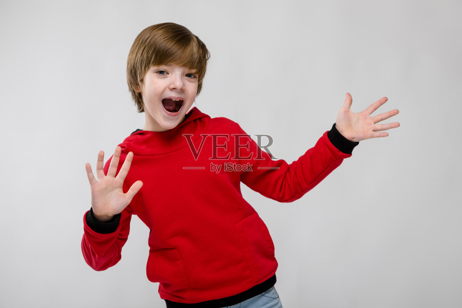 可爱自信的白人小男孩在红色毛衣显示打开手掌与张开的嘴在灰色的背景照片摄影图片