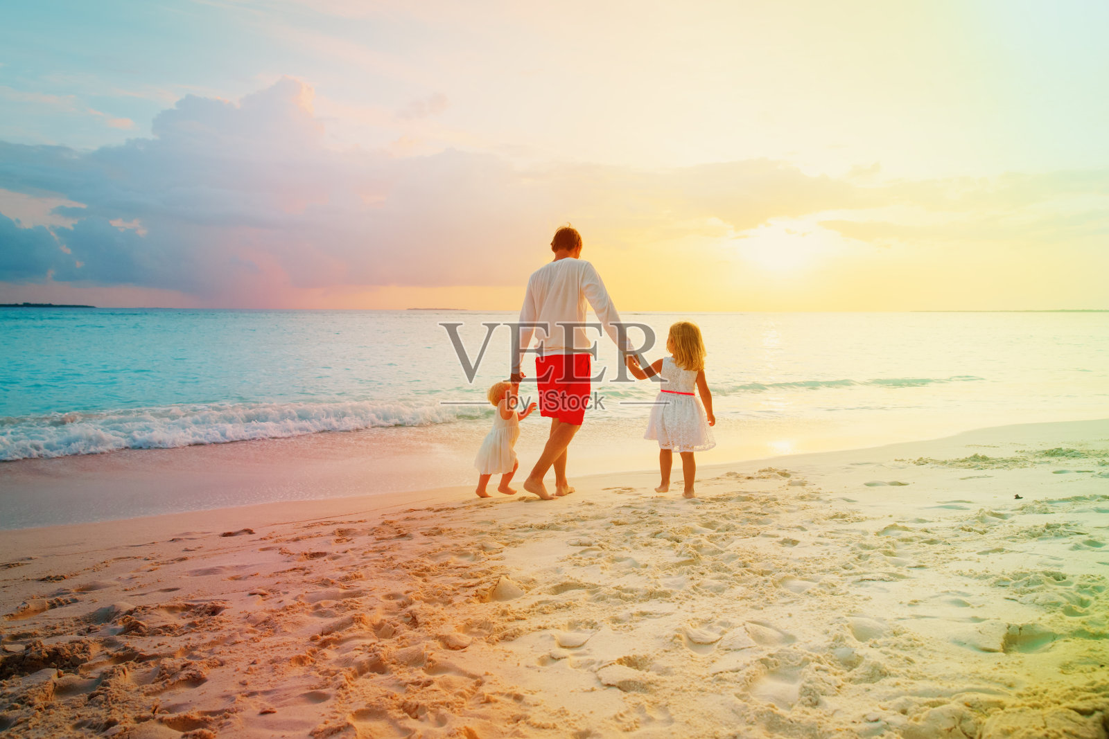 日落时分，父亲带着两个孩子在海滩上散步照片摄影图片