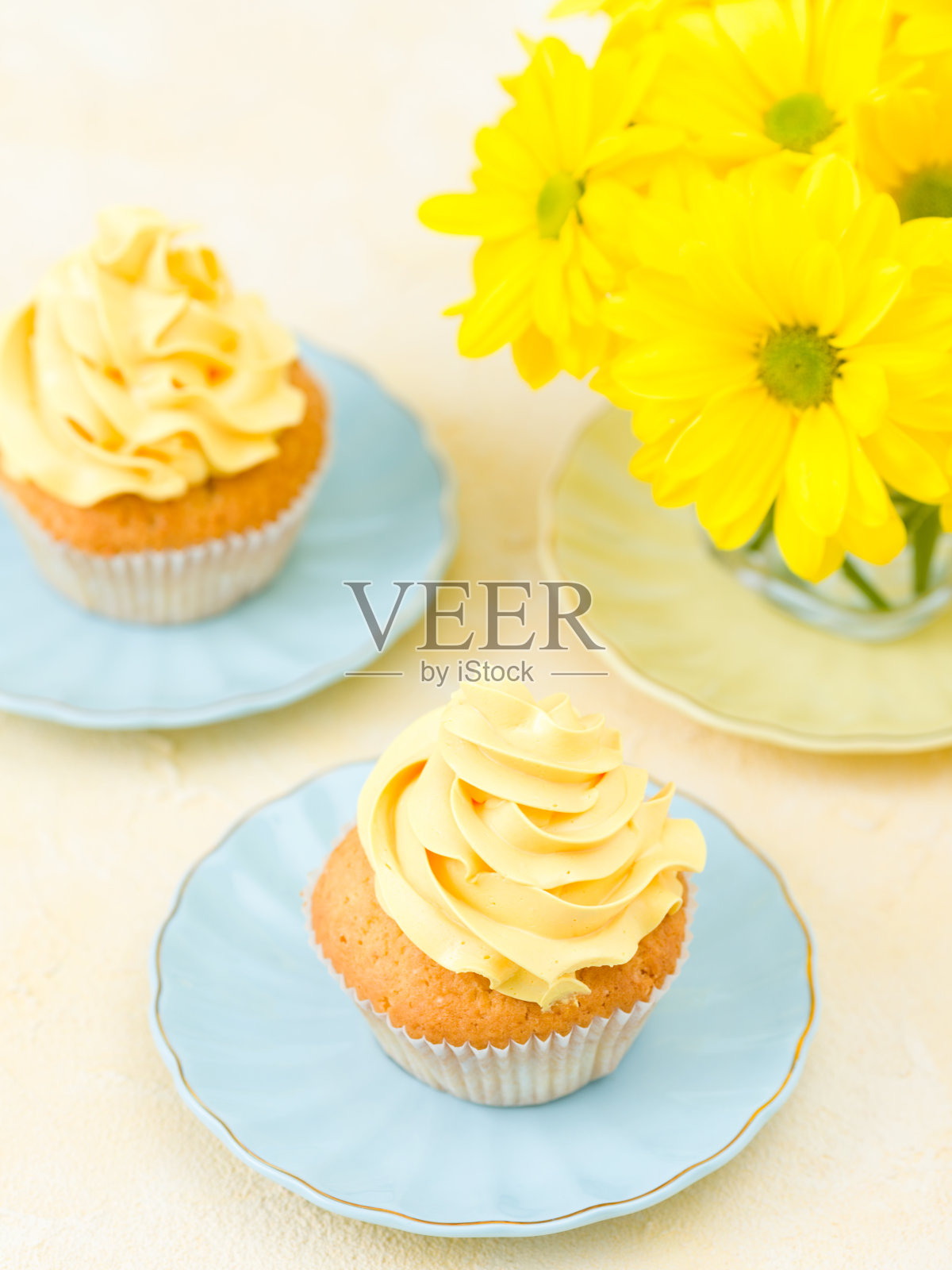 小杯子蛋糕，有黄色奶油装饰和一束黄色菊花。照片摄影图片
