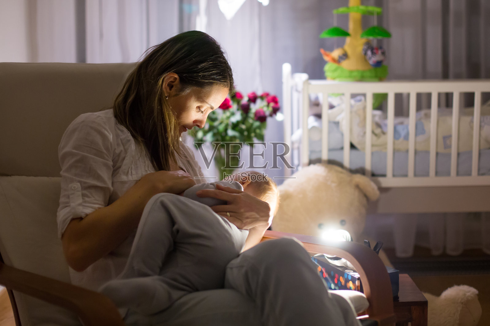 年轻美丽的母亲，在昏暗的灯光下给她的新生儿喂奶照片摄影图片