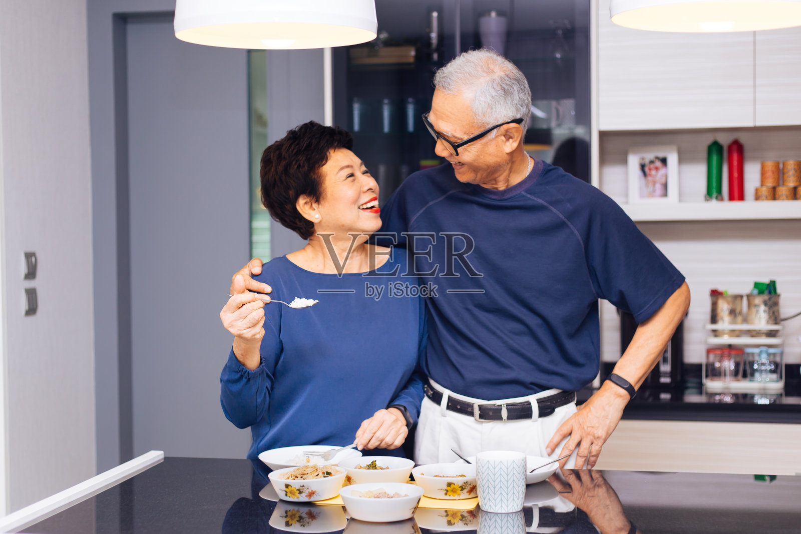 年长的亚洲夫妇祖父母一起做饭，而女人正在厨房给男人喂食物。持久关系概念照片摄影图片