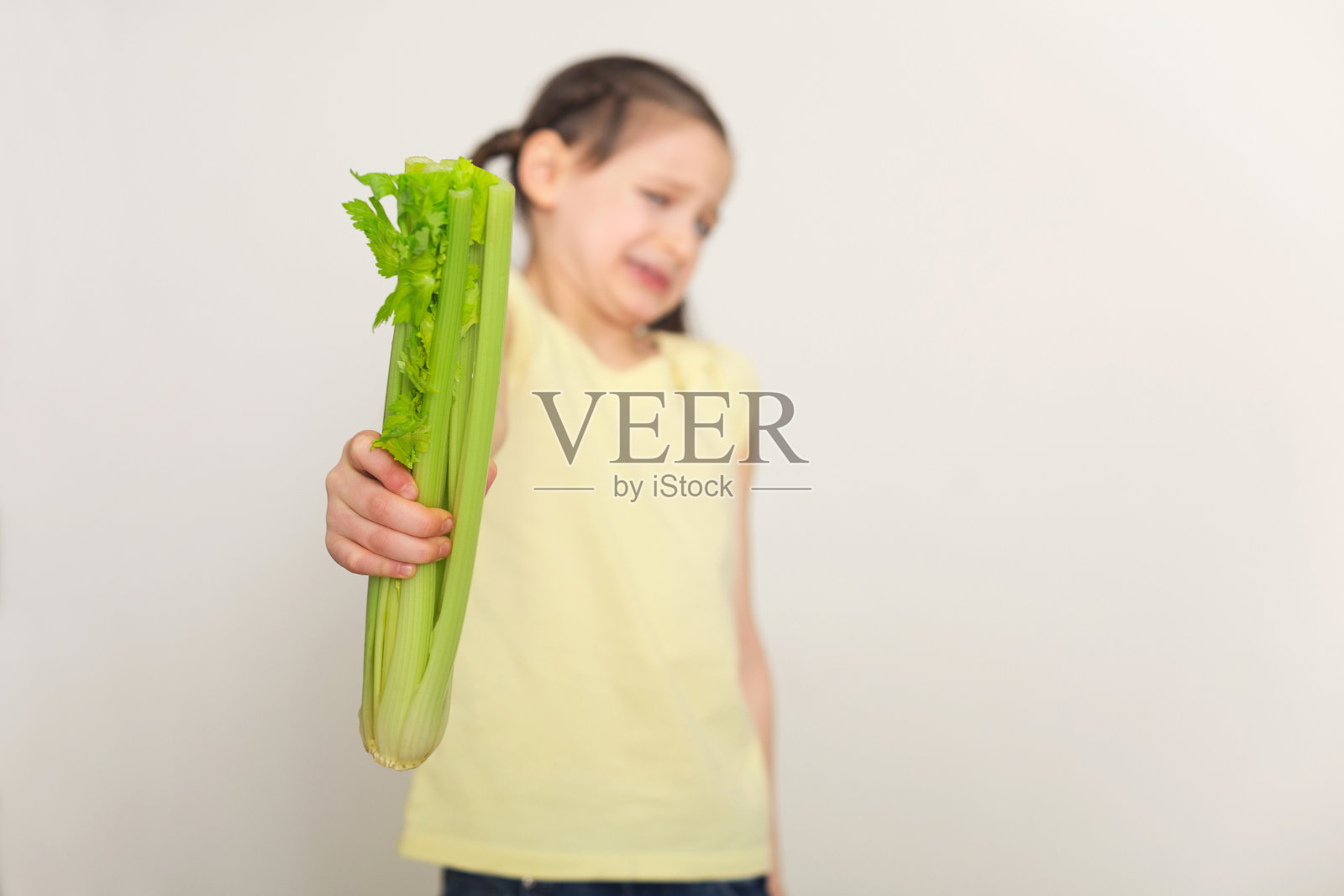 恶心的小女孩用芹菜在白色的背景照片摄影图片