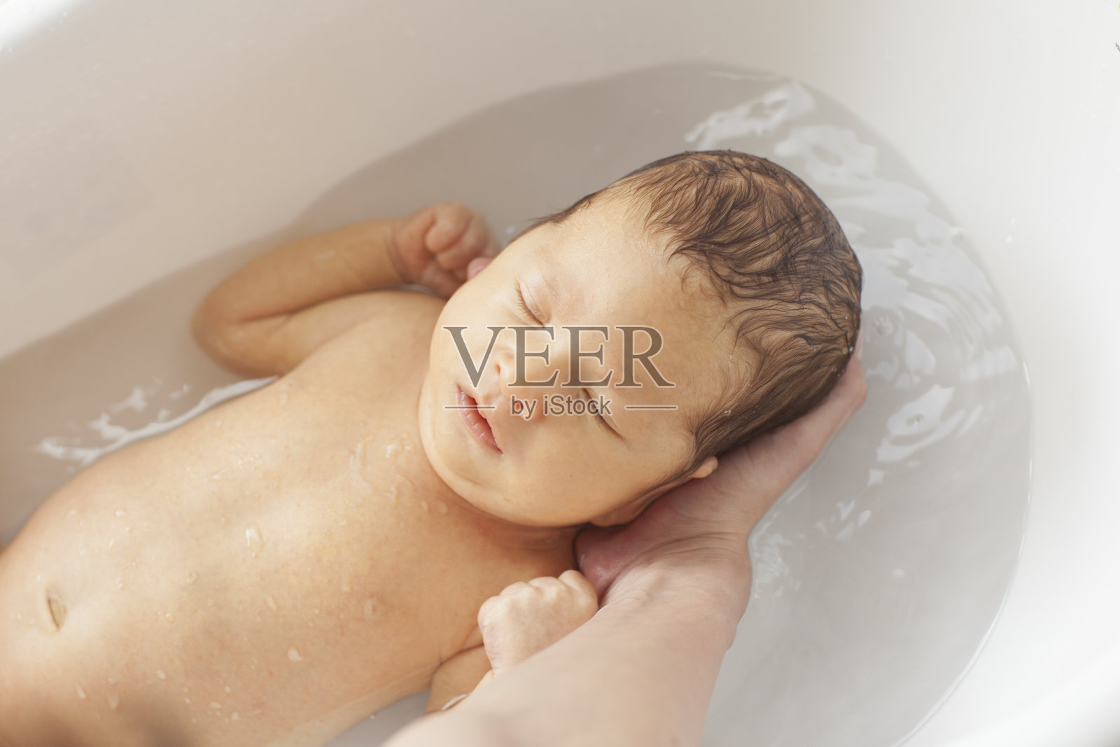 小婴儿在她妈妈的臂弯里洗澡。照片摄影图片