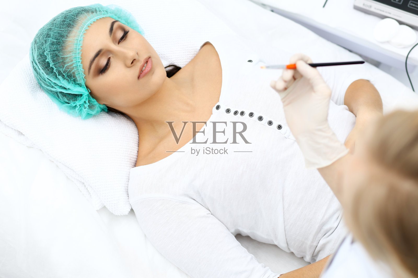 专业的美容师正在做美容手术在轻的医学背景下用刷子触摸病人的脸，特写。美容应用照片摄影图片