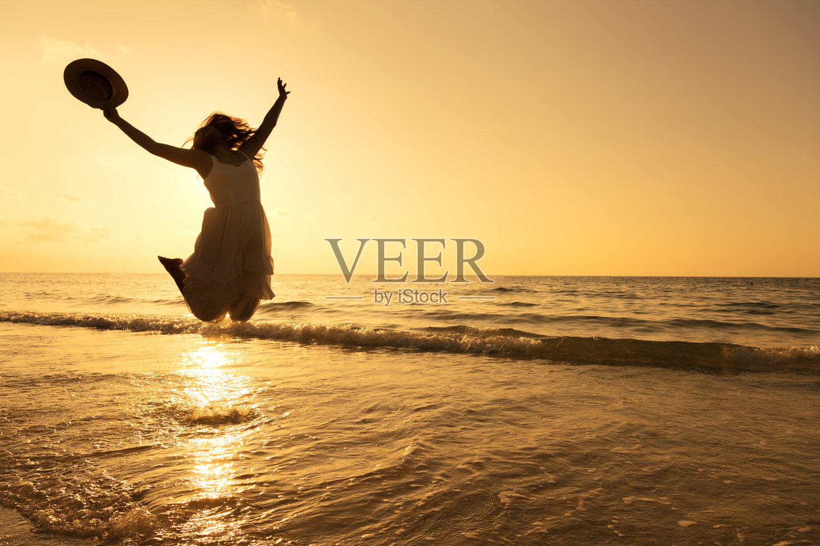 穿着白色连衣裙的漂亮女人的剪影是跳跃和放松在海滩上。积极的情感。夏天的概念。照片摄影图片