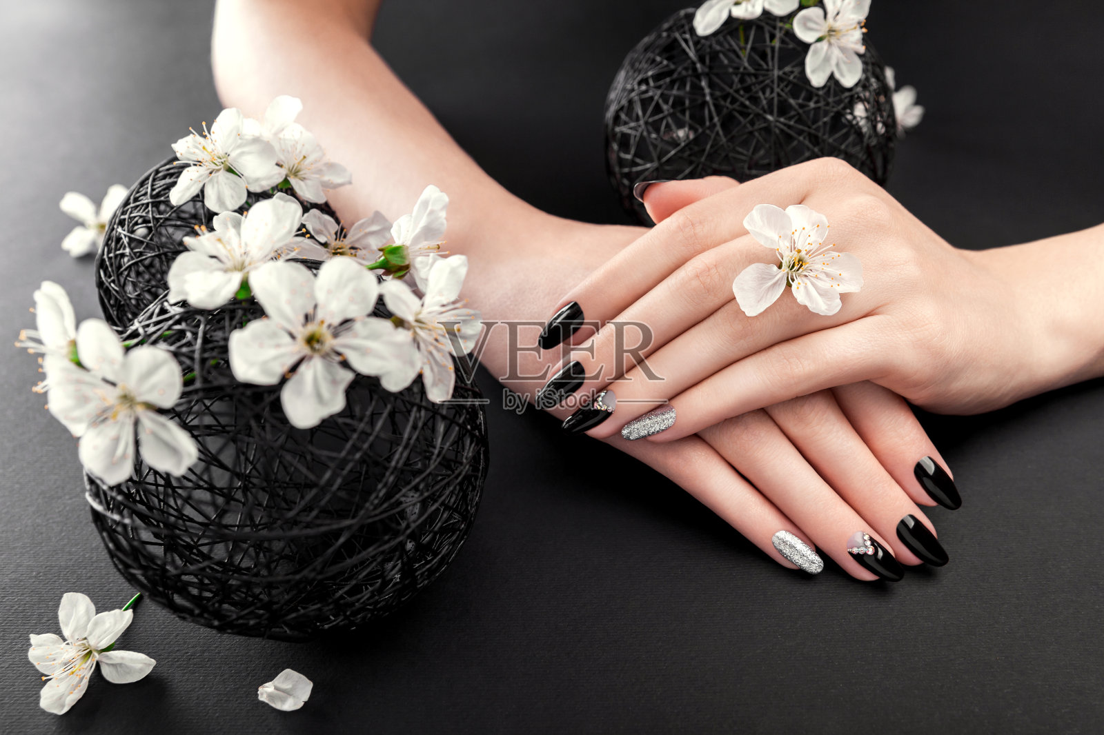 黑色和银色的美甲与樱花在黑色的背景。黑指甲，白花环绕的女人照片摄影图片
