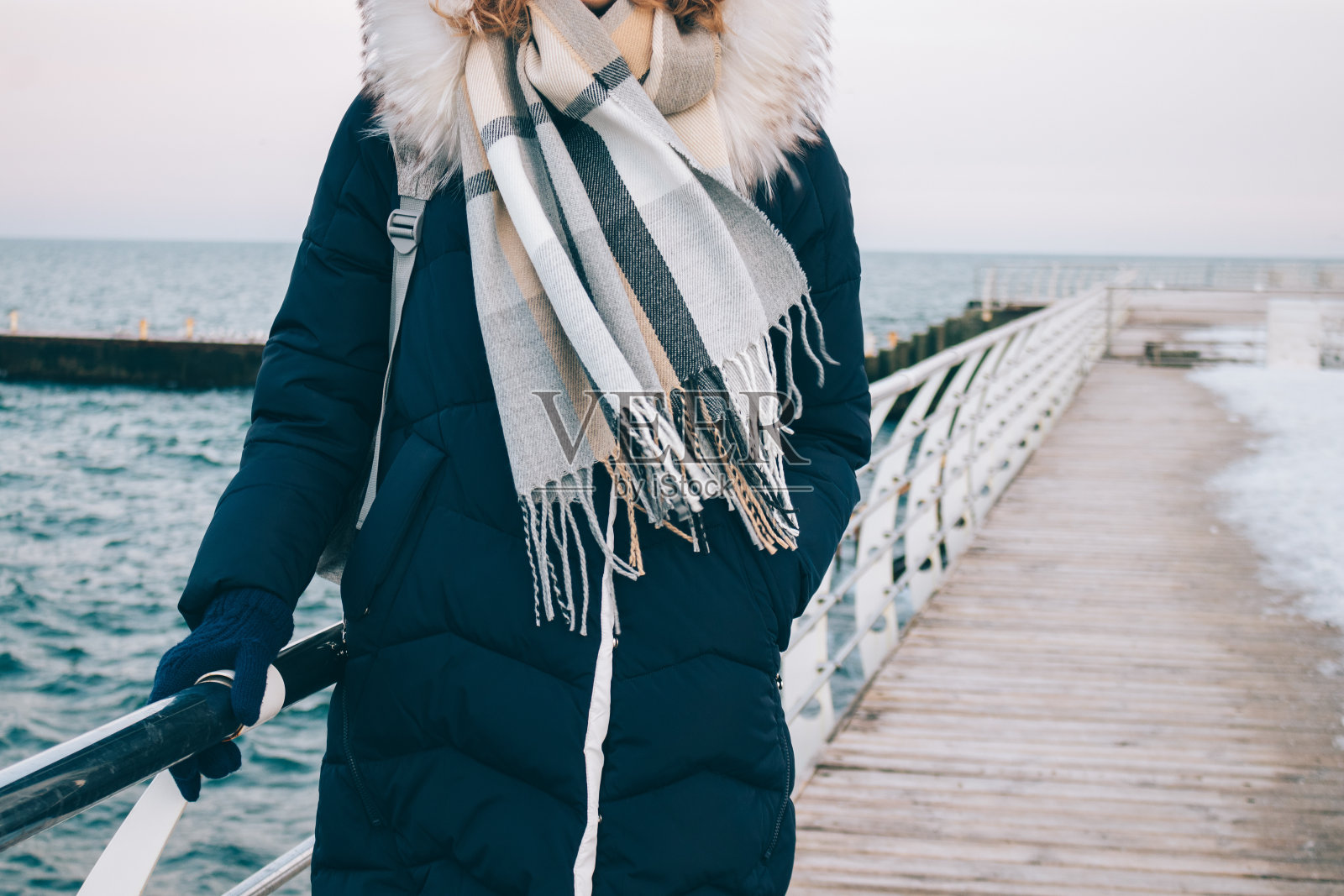 戴着围巾的年轻女子站在海边的冬季步行街上照片摄影图片