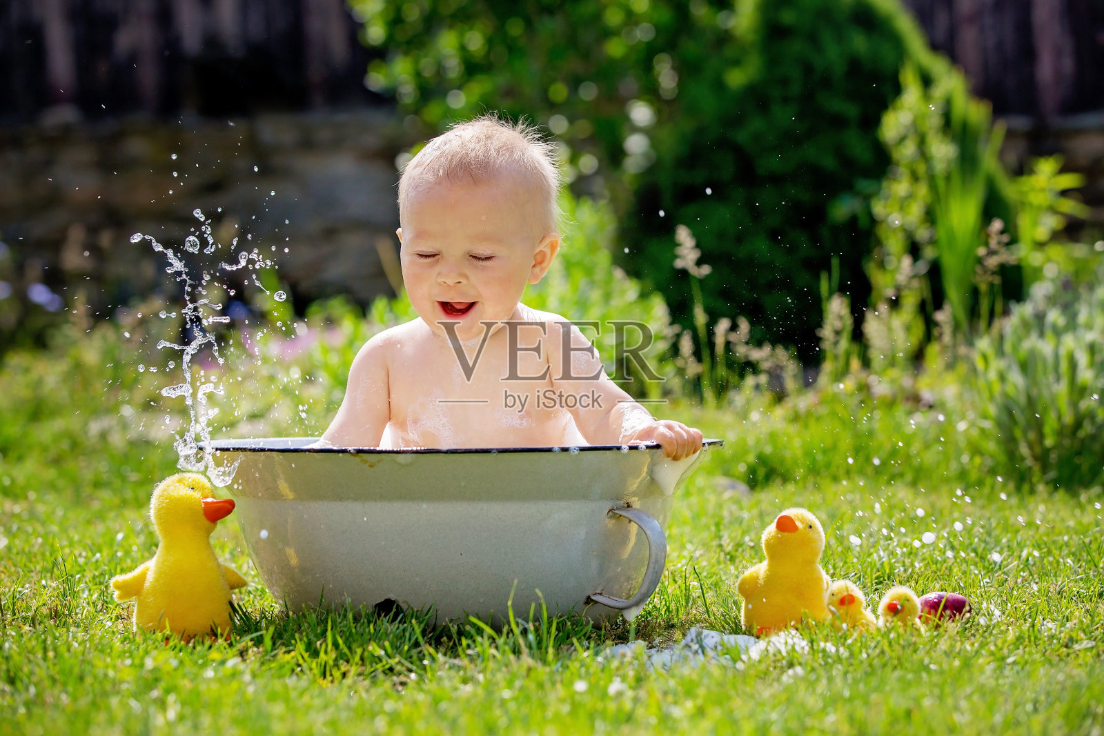 可爱的小男孩在水池里，在花园里用泡泡和鸭子玩具洗澡照片摄影图片