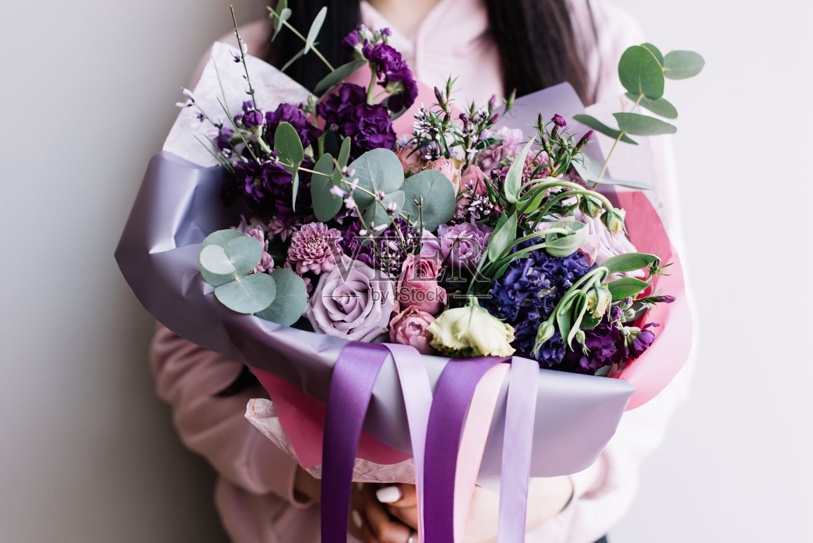 非常漂亮的年轻女子拿着一个大的美丽的鲜花盛开的玫瑰，马提奥拉，康乃馨，丁香，桉树在紫色的颜色在灰色的墙壁背景照片摄影图片