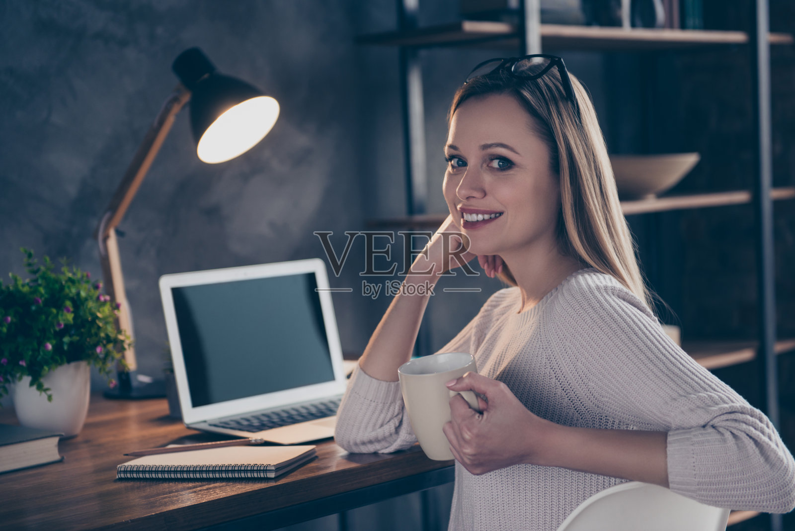企业程序员的肖像，聪明迷人的记者时尚的作家享受休息，喝着茶，手里拿着马克杯看着相机使用笔记本电脑的工作坐在桌面照片摄影图片