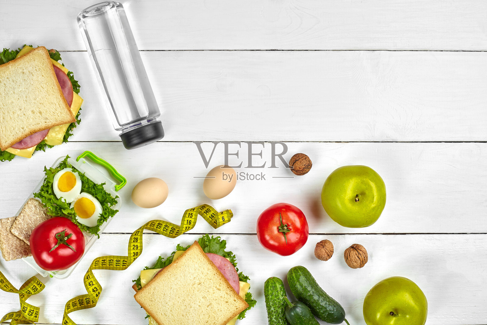 午餐。三明治和新鲜蔬菜，一瓶水，坚果和水果在白色的木制背景。健康饮食的概念。顶部视图与复制空间照片摄影图片