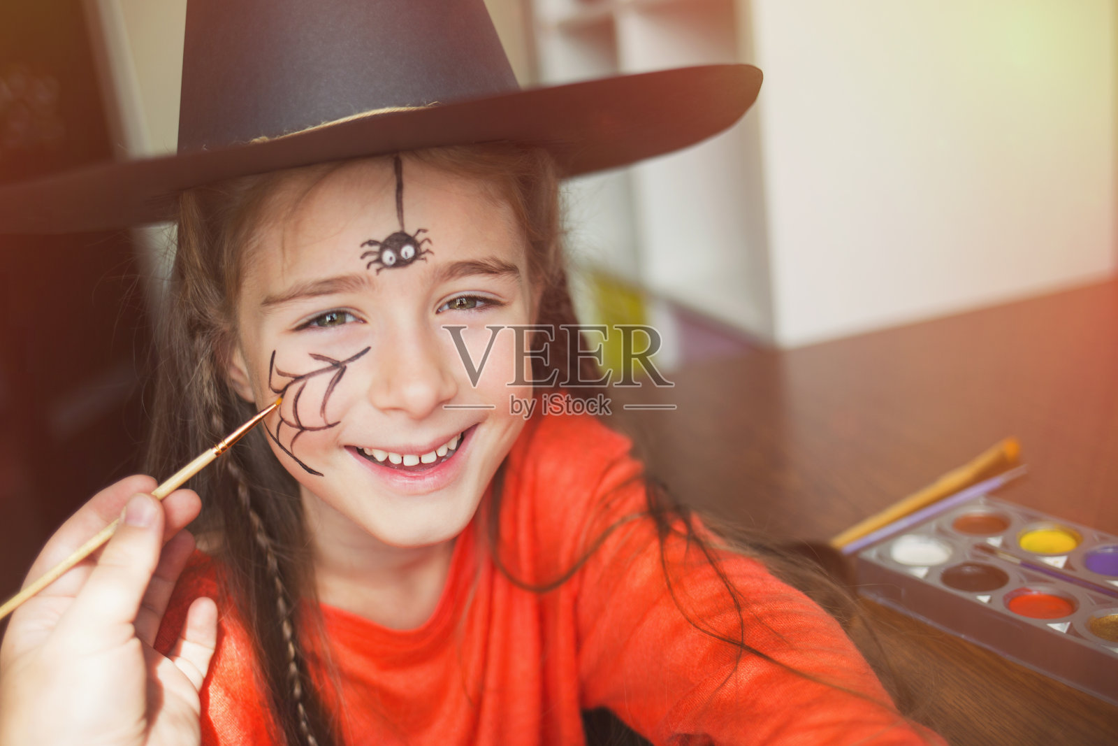 为万圣节做准备。穿着女巫服的孩子在做脸部彩绘。可爱的蜘蛛。简单套装的理念，diy照片摄影图片
