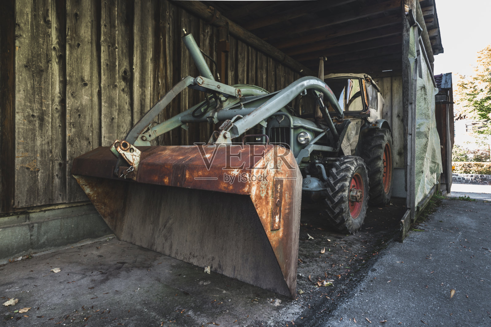德国巴伐利亚，一间深色木棚内，一辆旧绿松石色的Eicher拖拉机，吊臂和生锈的铁铲照片摄影图片