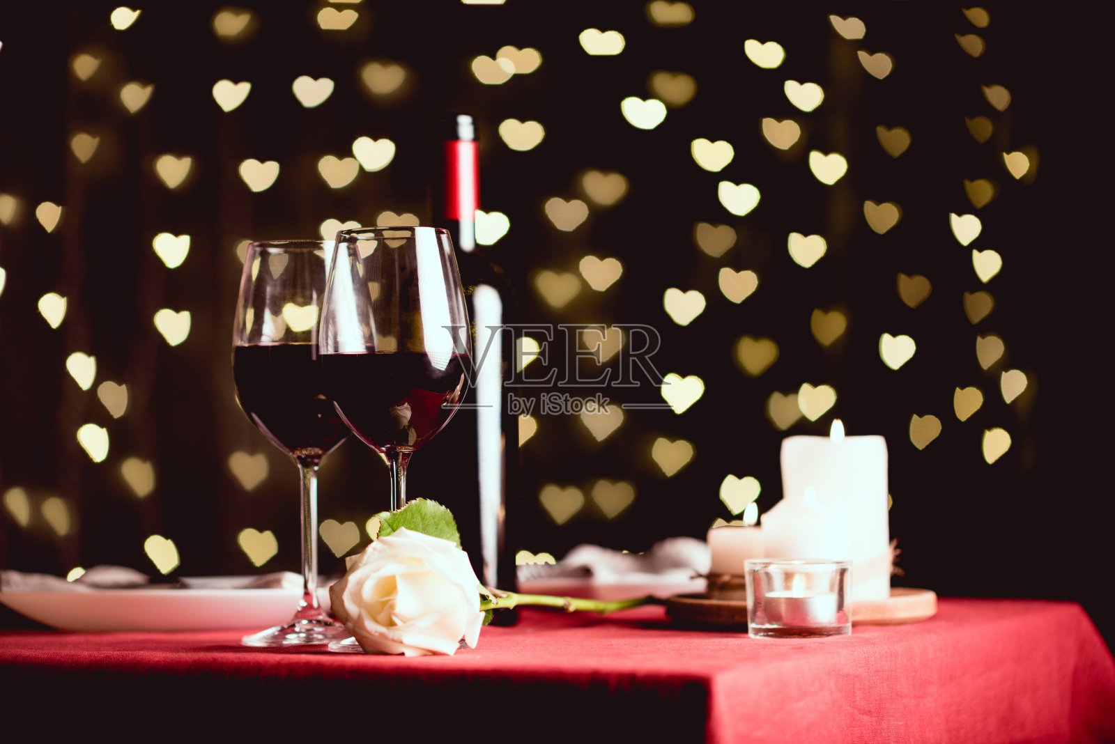 以红酒、玫瑰和心型散景为背景的餐桌摆设照片摄影图片