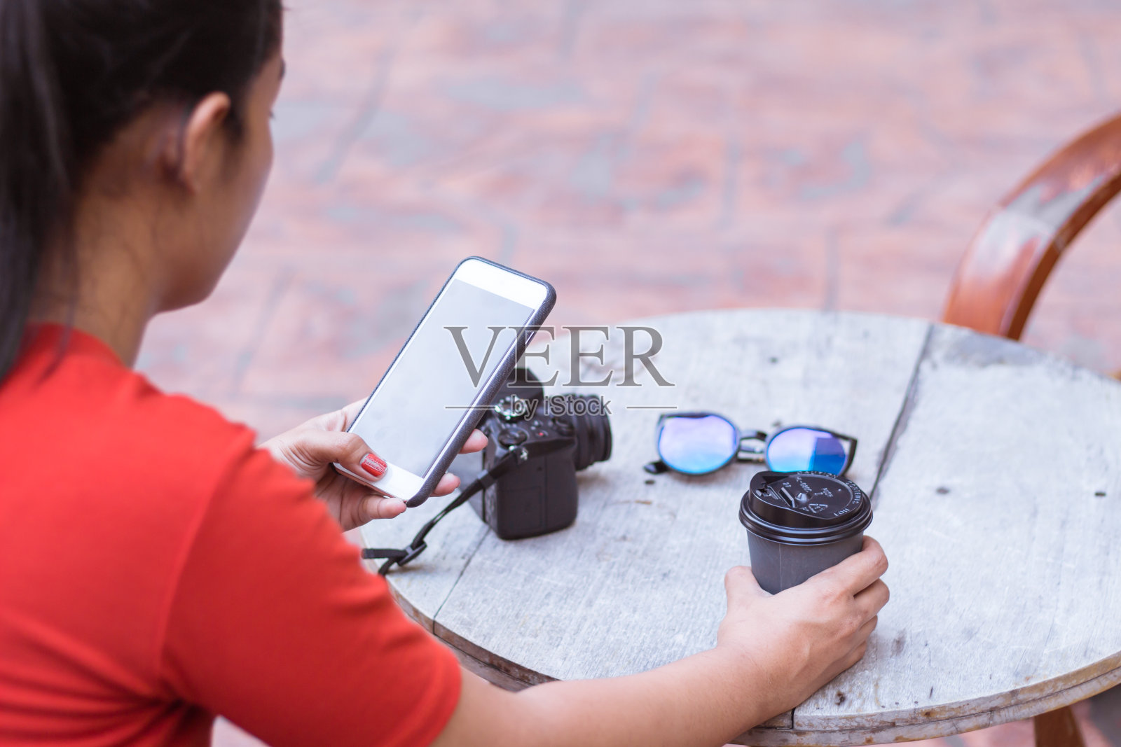 小女孩正在用手机玩网络，木桌上放着照相机、太阳镜、咖啡杯。照片摄影图片
