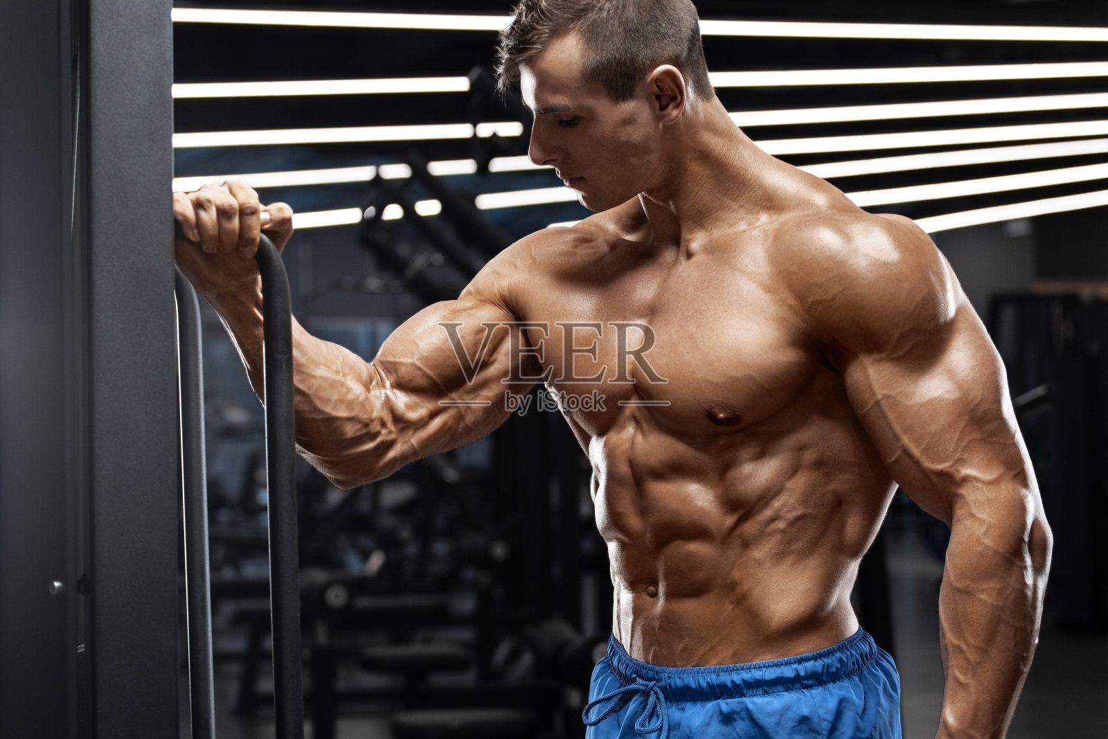 肌肉男在健身房锻炼显示二头肌。强壮的男性躯干腹肌照片摄影图片