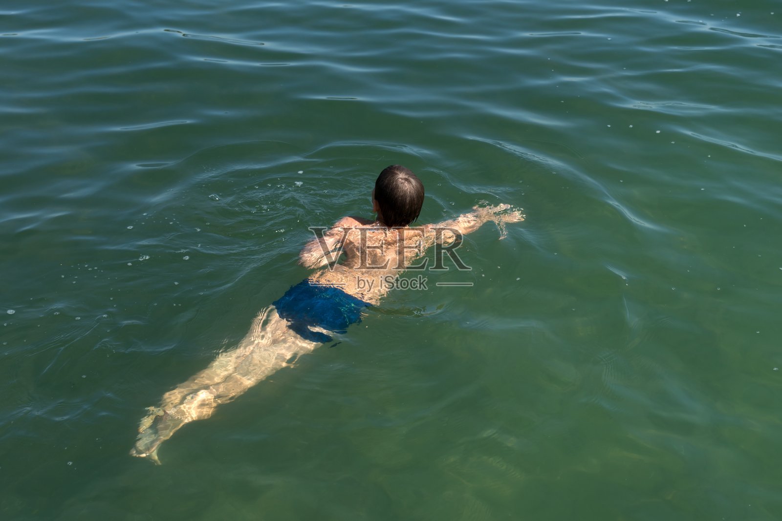 一个11岁的男孩正在一个天然水库的蓝色水中游泳。照片摄影图片