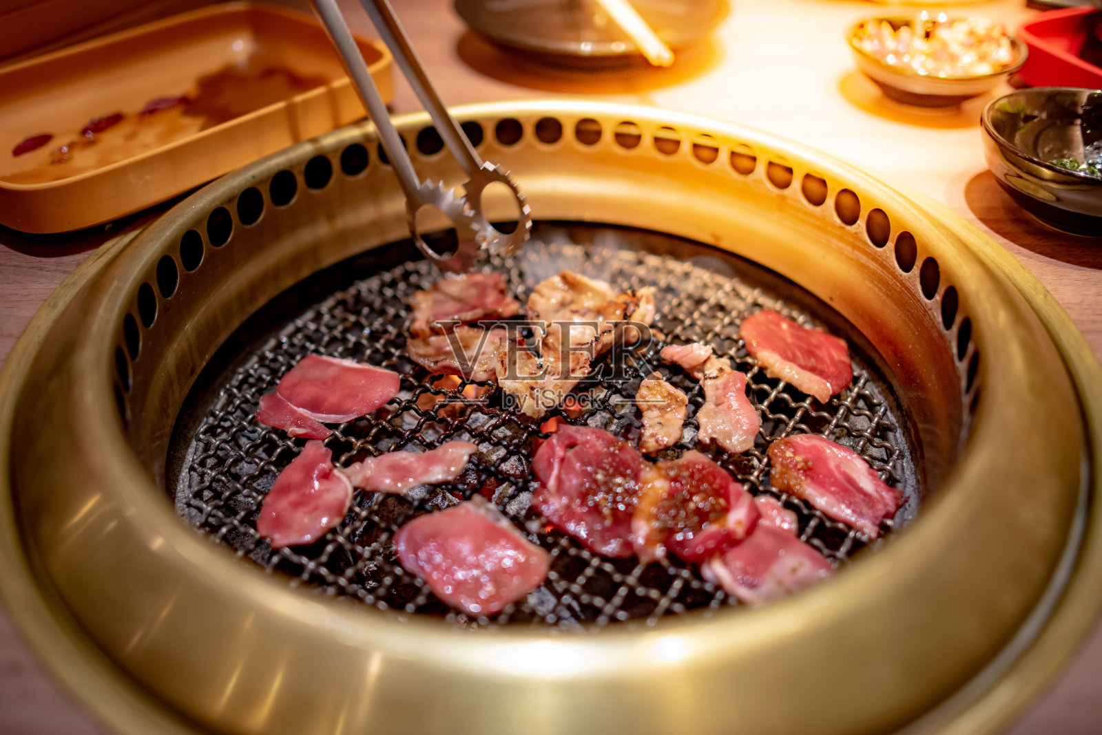 厨房用钳子在金色的炉子里烤着牛肉和培根。在餐厅享用韩国烧烤自助餐。照片摄影图片