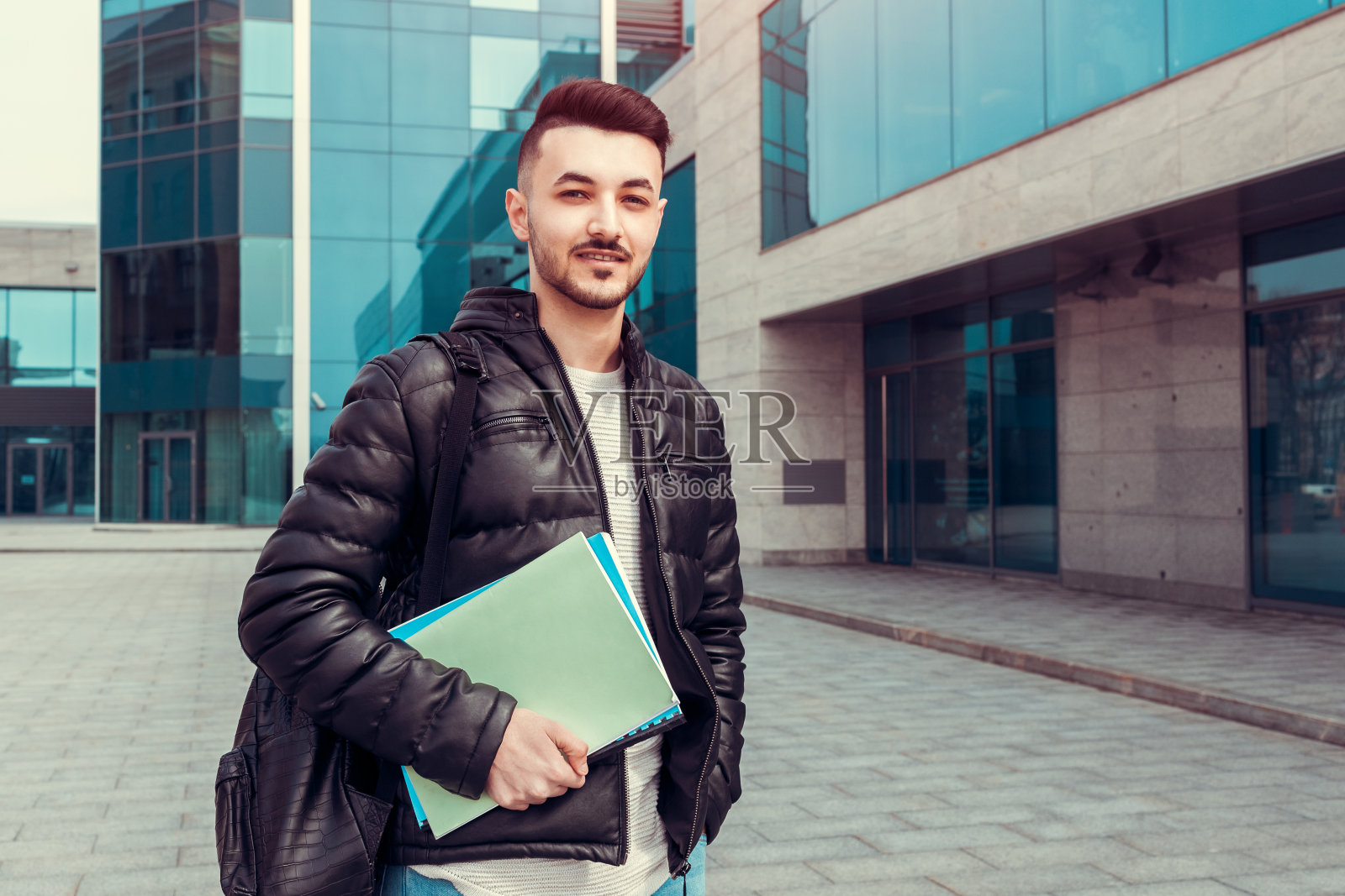 阿拉伯学生拿着抄本被现代大学外。一个背着背包看着相机的年轻人照片摄影图片