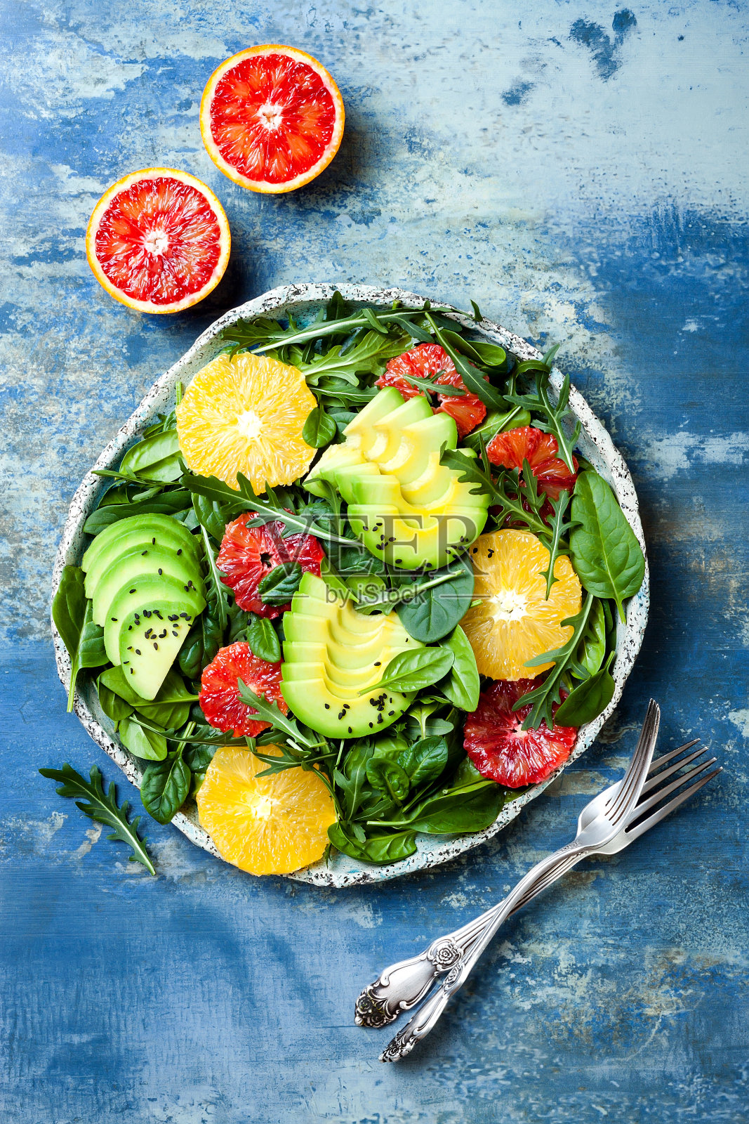 混合绿色蔬菜和血橙的柑橘沙拉。纯素、素食、清洁饮食、节食、饮食观念。蓝石头背景。照片摄影图片