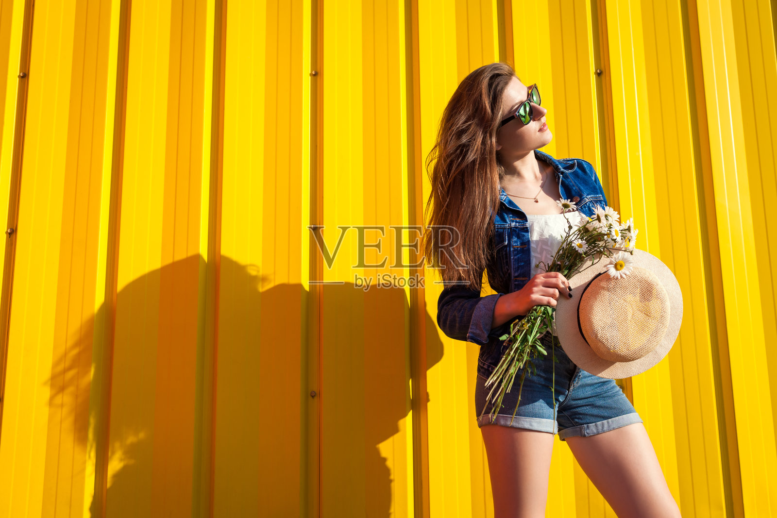 时髦女孩的肖像戴着眼镜和帽子与花反对黄色的背景。夏季服装。时尚。空间。照片摄影图片