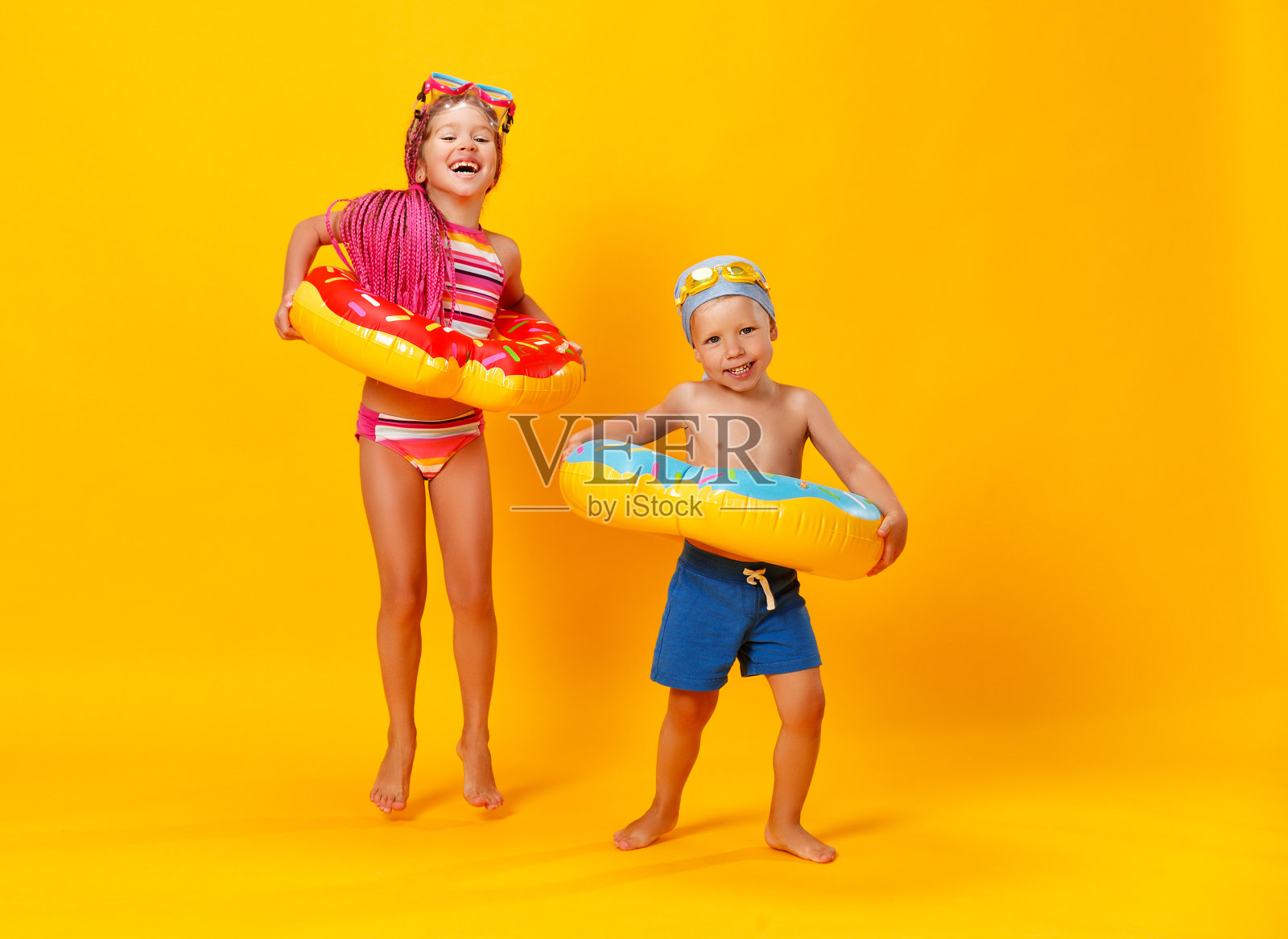 快乐的孩子女孩和男孩在泳衣与游泳圈甜甜圈在彩色黄色的背景照片摄影图片