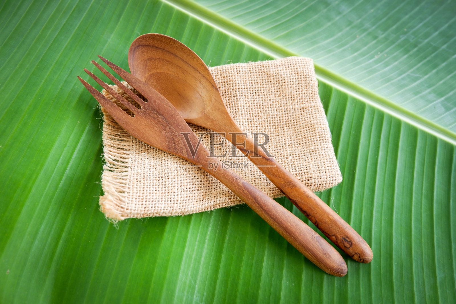 木制的勺子和叉子厨房用具设置在麻袋香蕉叶的背景下/零浪费使用更少的塑料的概念照片摄影图片