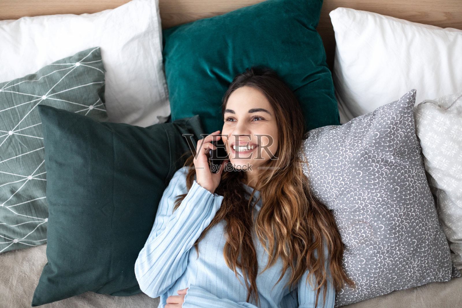 幸福的女人在家里的床上打电话。照片摄影图片