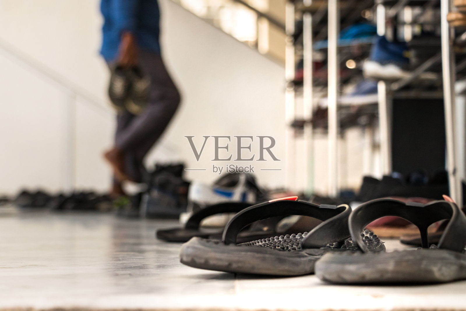 马尔代夫马累一座清真寺的正门外放着凉鞋，一名祈祷者正在脱鞋，背景模糊照片摄影图片