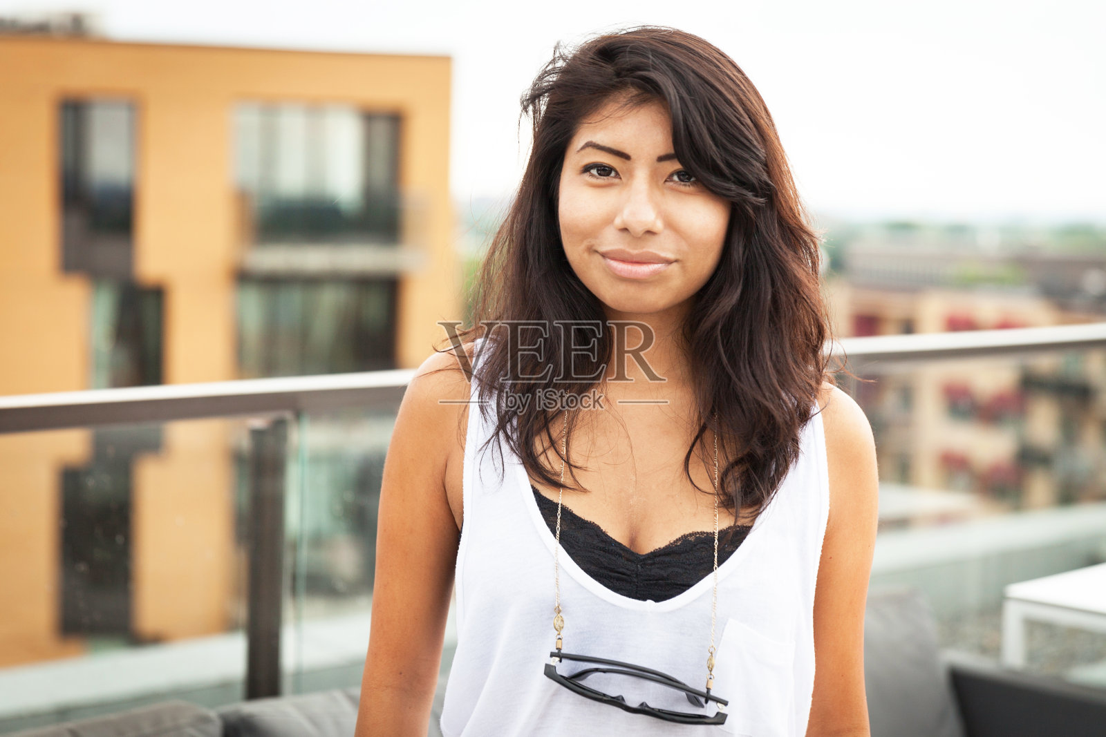 年轻的拉丁女人对着镜头微笑。她在外面一幢大楼的顶上。照片摄影图片