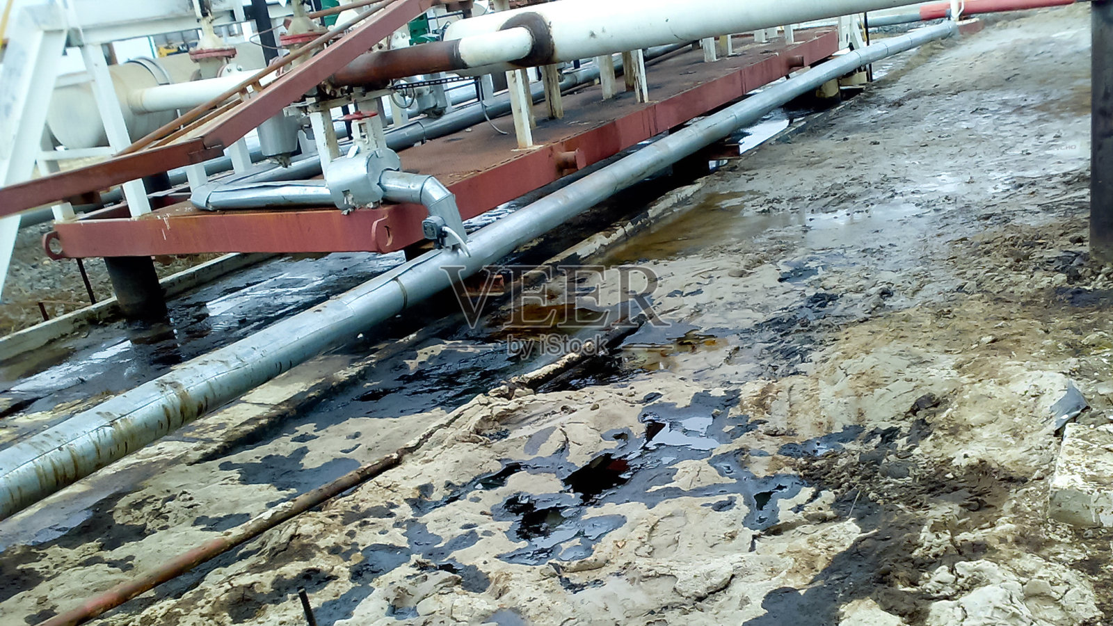 泄漏的石油在管道和工艺设备附近的沙土上。操作和维修过程中发生漏油。照片摄影图片