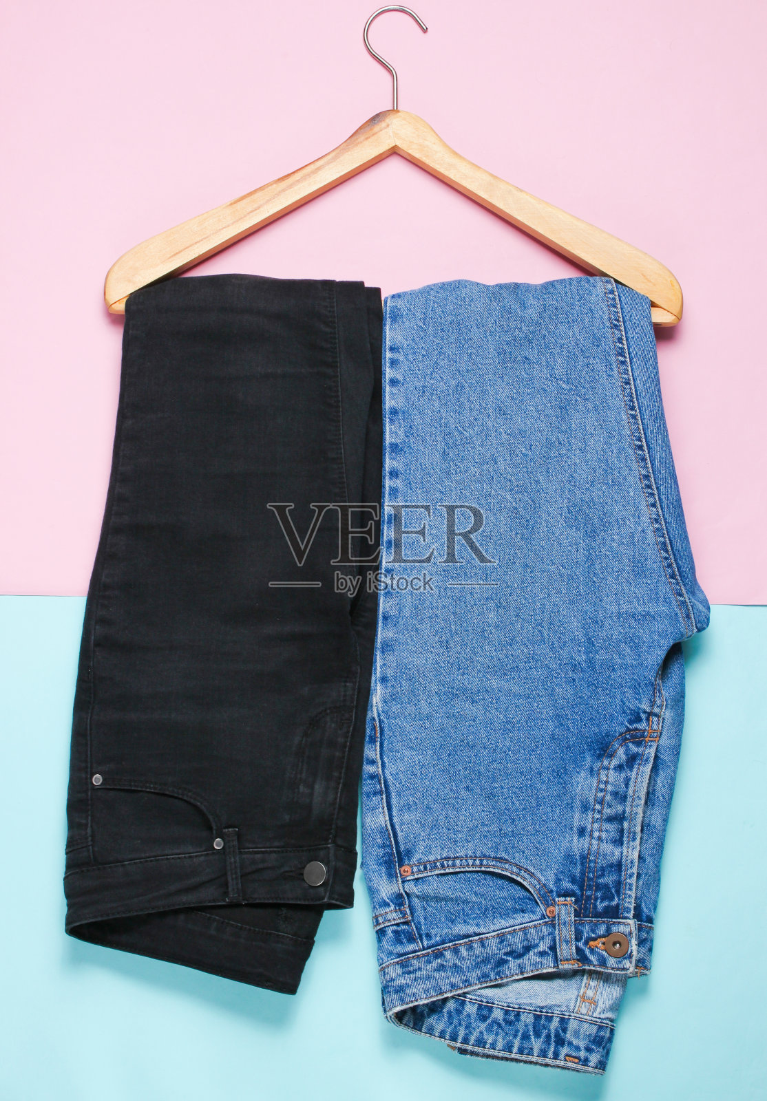 俯视图，平铺两条黑色和蓝色的牛仔裤，一个木制衣架在柔和的背景。极简主义照片摄影图片