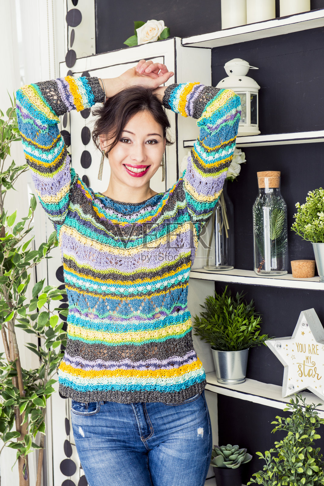这个快乐的女人穿着一件手工毛衣在室内摆姿势，这是一件用针编织的时髦套衫照片摄影图片