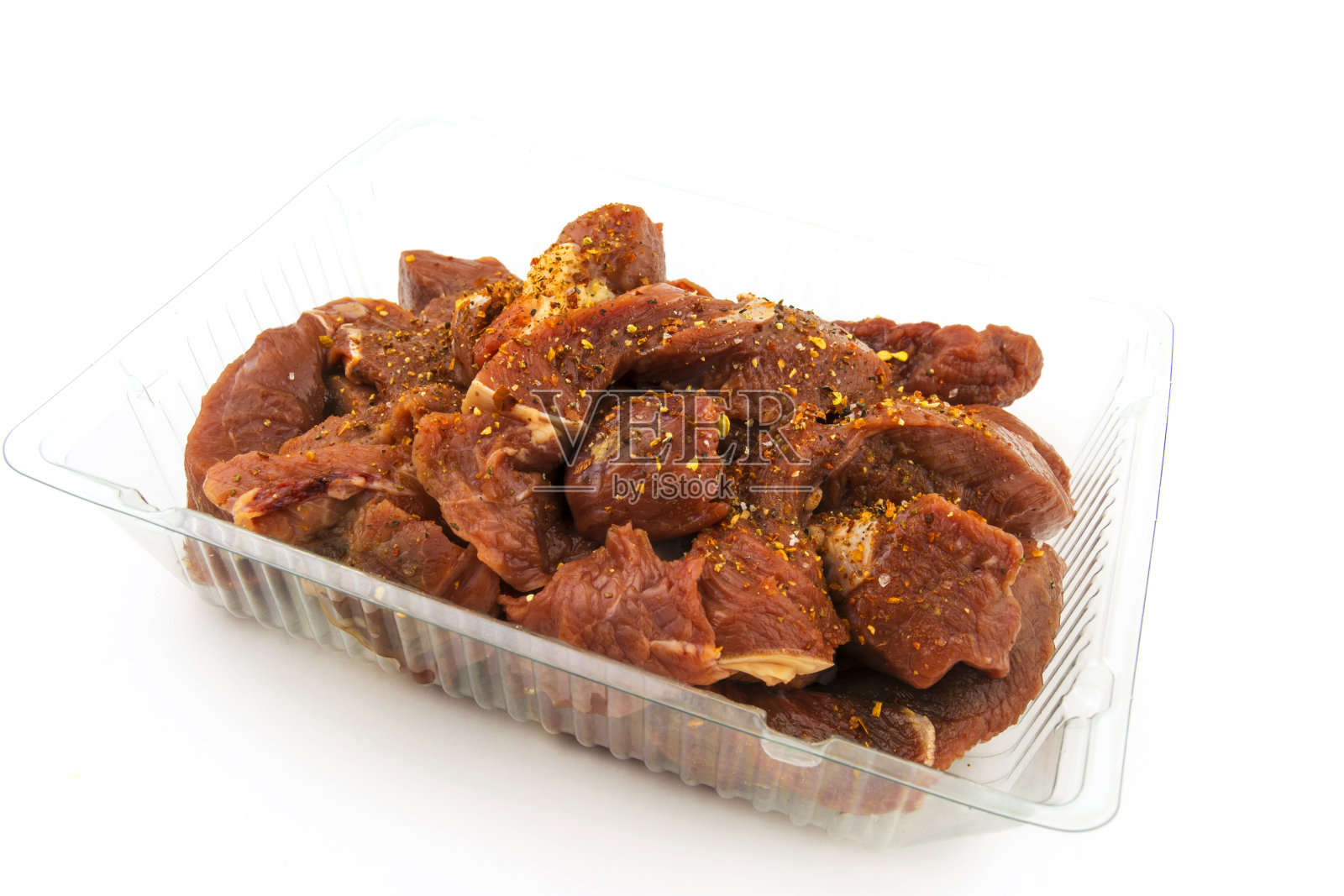 生牛肉片，炖牛肉放在一个塑料托盘里，撒上香料。在白色背景上。照片摄影图片