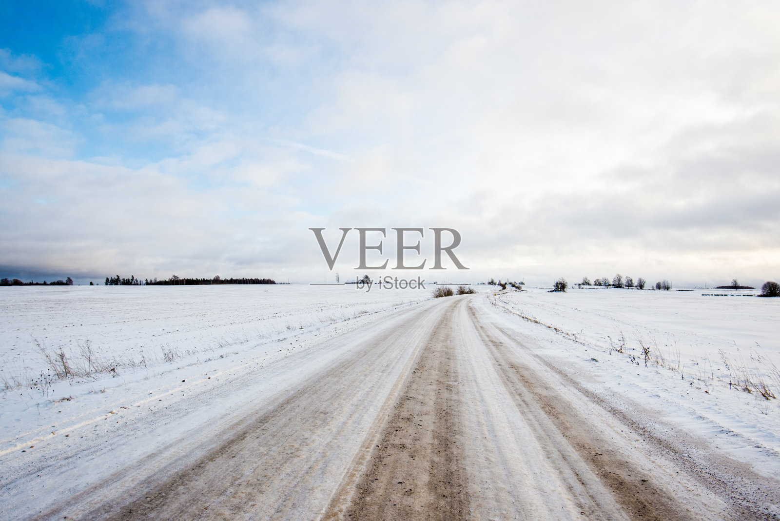 日落时分，一条穿过白雪覆盖的田野的路。阳光明媚的冬日照片摄影图片