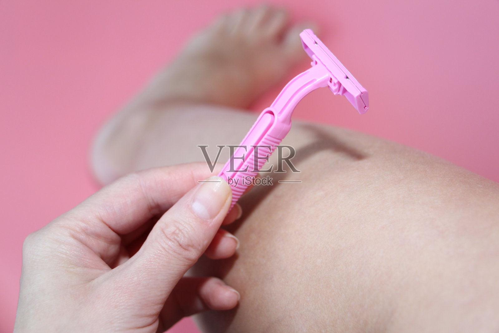 美丽的女性手拿着一个粉红色的剃刀在腿的背景。照片摄影图片