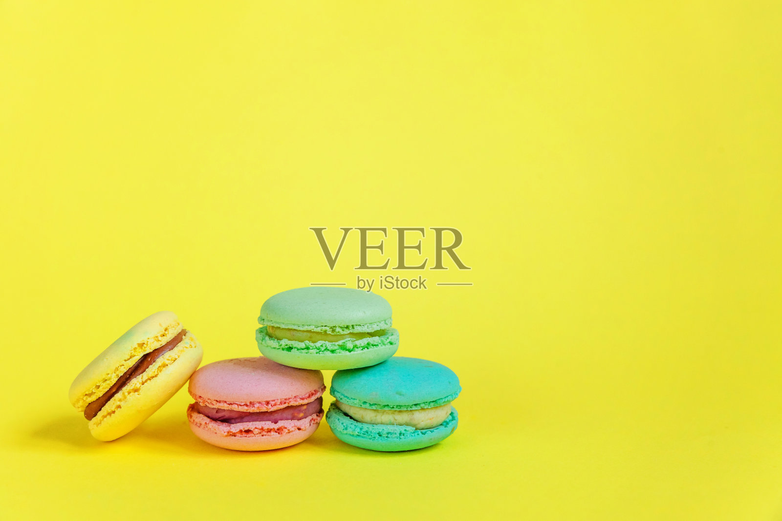 法国甜的饼干。简约的食品烘焙概念。粉蓝黄绿的马卡龙在黄色的背景上照片摄影图片