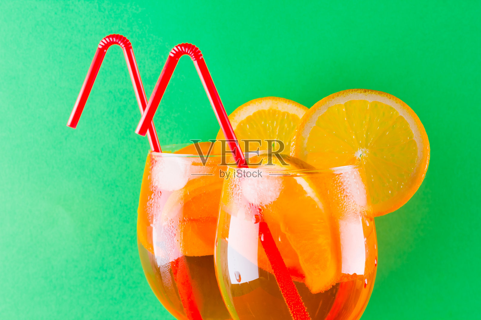 鸡尾酒喷在红绿背景上。夏日酒精鸡尾酒配橙子片。喷上彩色背景。极简主义风格的珊瑚色鸡尾酒照片摄影图片