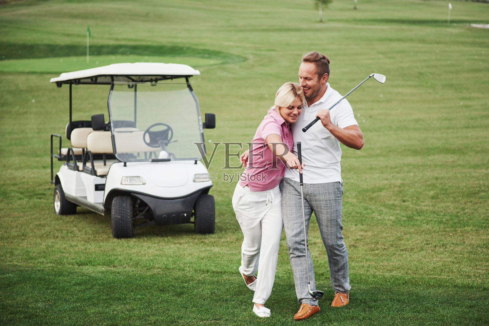 两名职业高尔夫球手，一男一女一起去下一个洞。情侣们拥抱微笑，他们有了约会照片摄影图片