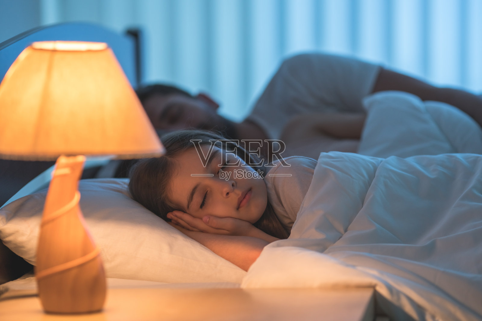 小女孩睡在父母旁边的床上。晚上的时间照片摄影图片