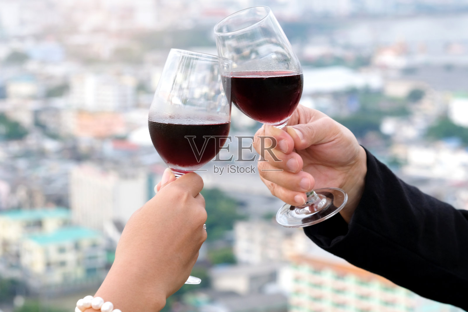 持续情侣在餐厅的露台上浪漫的晚餐时间，手握红酒和散景灯，夜晚的城市背景。情人节的概念，晚餐的概念。照片摄影图片