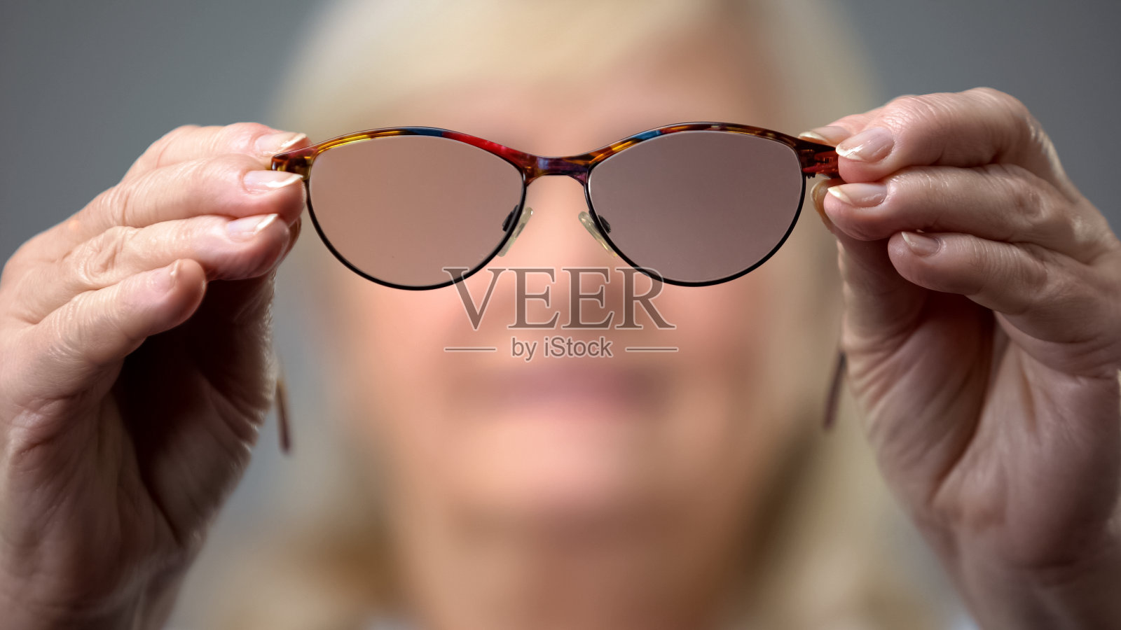 老妇人拿着时髦的眼镜，观念视力有问题，背景模糊照片摄影图片