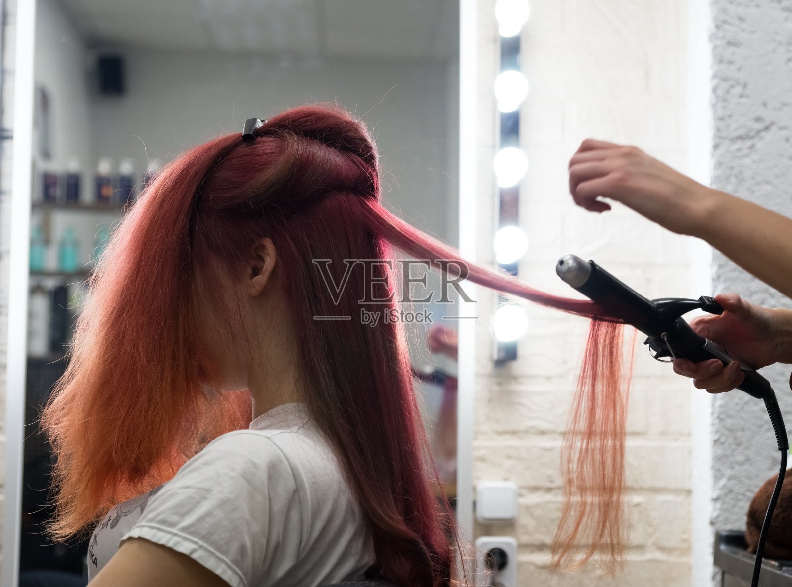 一个长头发的女人坐在卷发程序卷发在沙龙理发师使用卷发器。照片摄影图片